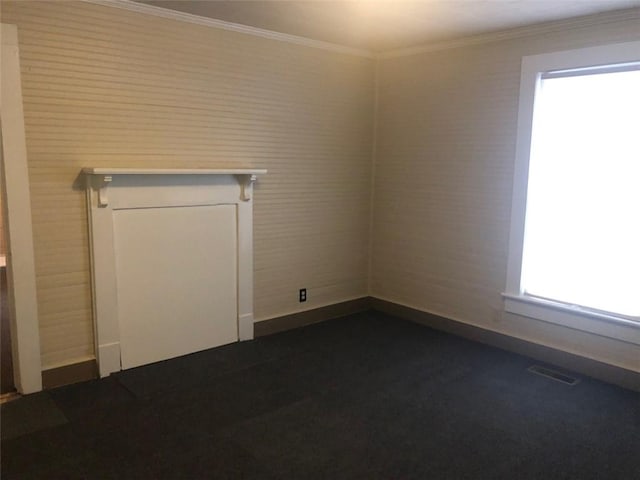spare room with baseboards, visible vents, ornamental molding, and dark colored carpet