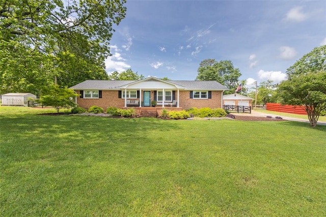 view of front of house featuring covered porch, a front yard, brick siding, and an outbuilding