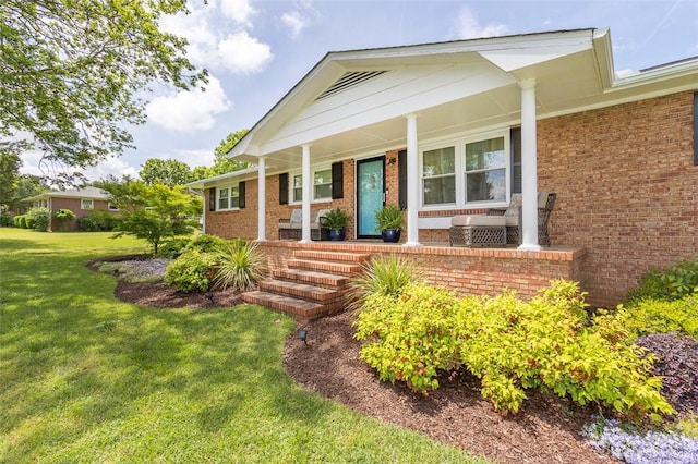 view of exterior entry featuring a lawn, a porch, and brick siding