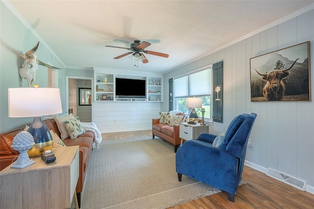 living room featuring built in features, crown molding, a ceiling fan, visible vents, and wood finished floors