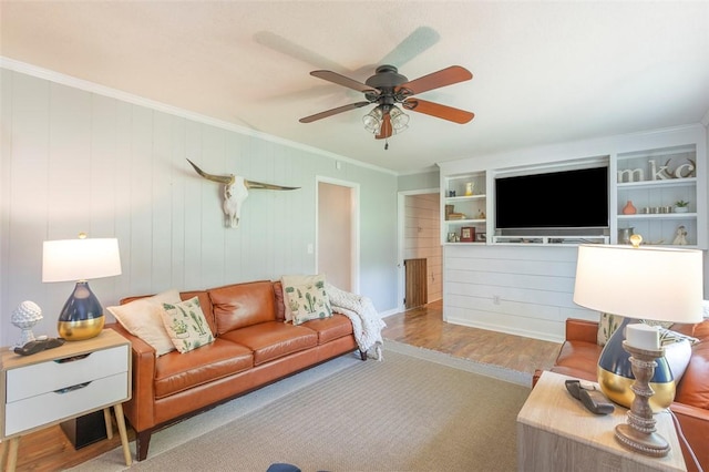 living room with built in shelves, ornamental molding, ceiling fan, and wood finished floors