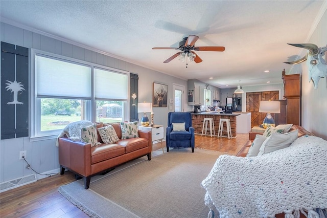 living area featuring light wood-style floors, ornamental molding, baseboards, visible vents, and a ceiling fan