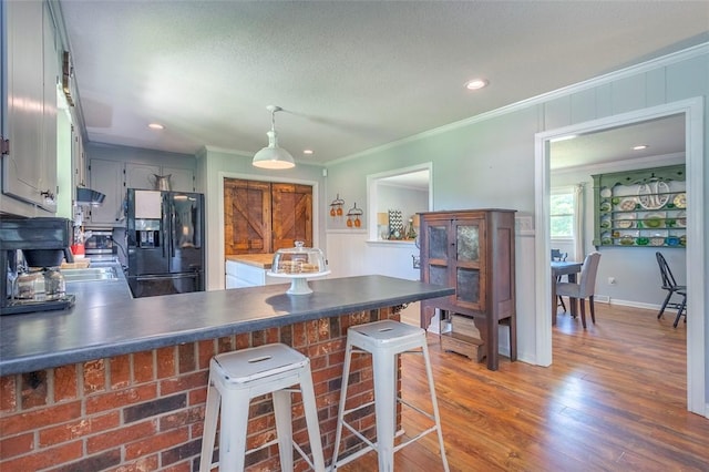 kitchen with dark countertops, black refrigerator with ice dispenser, ornamental molding, and a peninsula