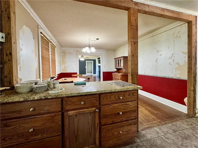 kitchen featuring brown cabinetry, ornamental molding, baseboards, a notable chandelier, and a textured ceiling