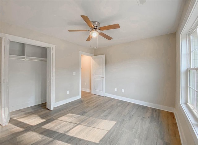 unfurnished bedroom featuring baseboards, multiple windows, wood finished floors, and a closet