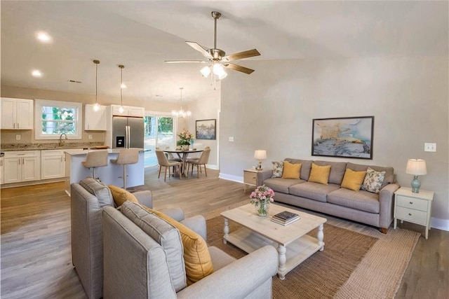 living area featuring baseboards, light wood-style flooring, ceiling fan with notable chandelier, and vaulted ceiling