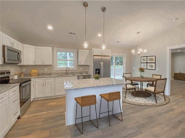 kitchen with an inviting chandelier, a kitchen island, white cabinets, a sink, and stainless steel appliances