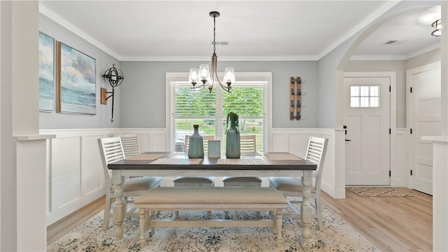 dining area featuring light wood finished floors, a decorative wall, a chandelier, visible vents, and ornamental molding