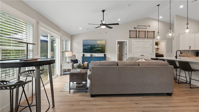 living area featuring light wood-style floors, high vaulted ceiling, ceiling fan, and wainscoting