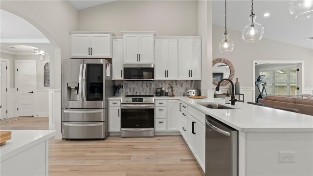 kitchen featuring lofted ceiling, tasteful backsplash, a sink, light wood-style flooring, and appliances with stainless steel finishes