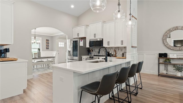 kitchen featuring a sink, arched walkways, high vaulted ceiling, stainless steel appliances, and white cabinetry