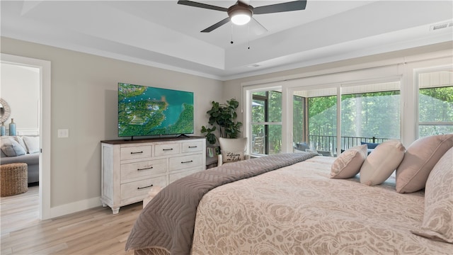 bedroom featuring light wood finished floors, access to exterior, baseboards, a tray ceiling, and visible vents
