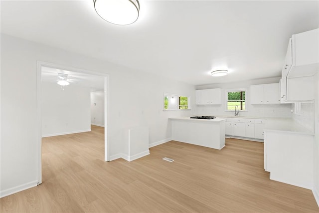 kitchen with a peninsula, baseboards, light wood-type flooring, light countertops, and white cabinets