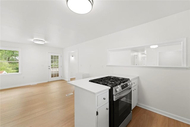 kitchen featuring white cabinets, light countertops, gas range, baseboards, and light wood-type flooring