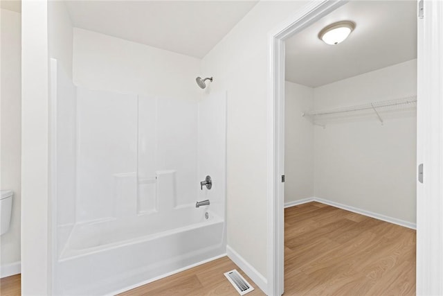 full bath featuring a walk in closet, visible vents, bathtub / shower combination, wood finished floors, and baseboards