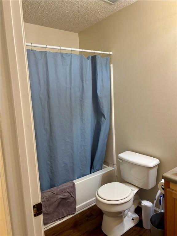 full bath featuring vanity, toilet, a textured ceiling, shower / bath combo with shower curtain, and wood finished floors
