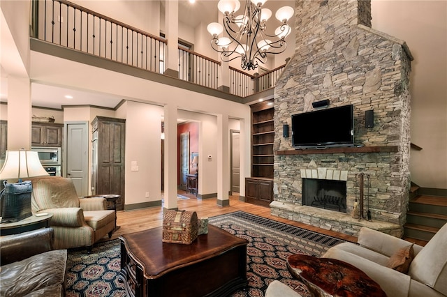 living room featuring a stone fireplace, built in shelves, light wood-style flooring, baseboards, and a towering ceiling