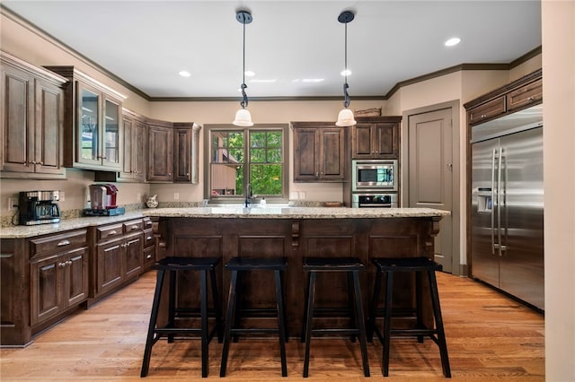 kitchen with dark brown cabinets, light wood-style floors, built in appliances, a center island, and ornamental molding