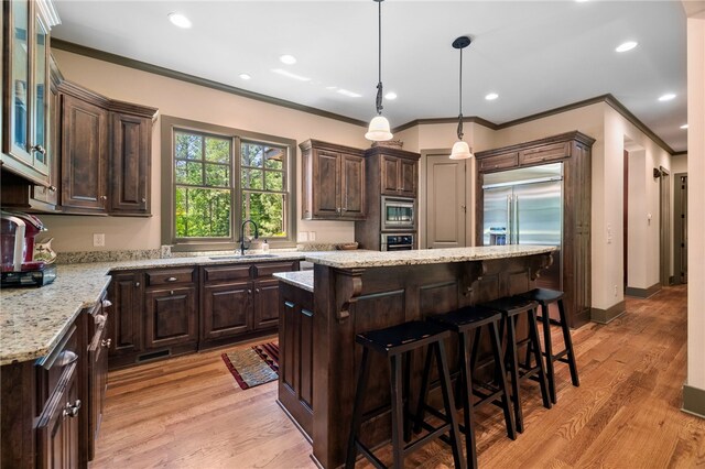 kitchen with crown molding, built in appliances, dark brown cabinetry, a center island, and a sink