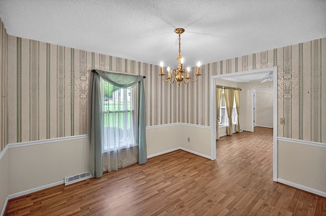 unfurnished dining area with a chandelier, baseboards, wallpapered walls, wood finished floors, and visible vents