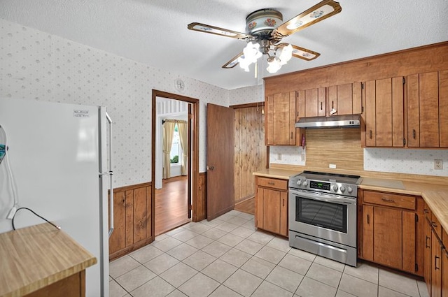 kitchen featuring brown cabinetry, stainless steel range with electric stovetop, freestanding refrigerator, under cabinet range hood, and wallpapered walls
