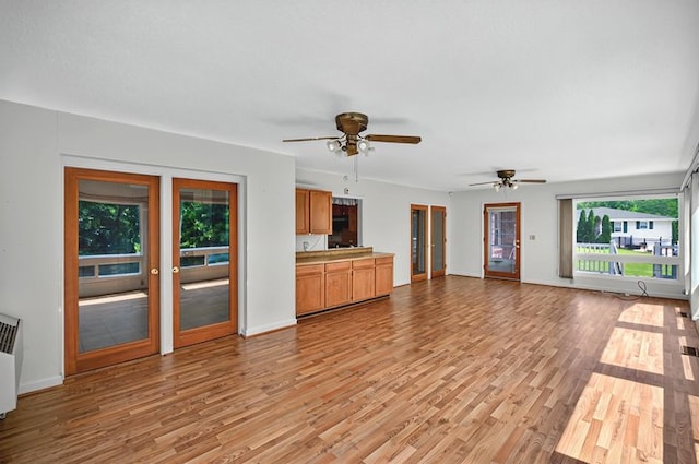 unfurnished living room with a ceiling fan, baseboards, and light wood finished floors