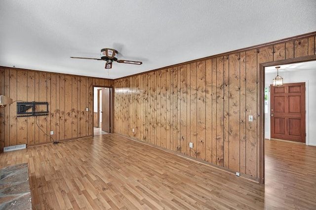 empty room with wooden walls, ceiling fan, visible vents, and wood finished floors