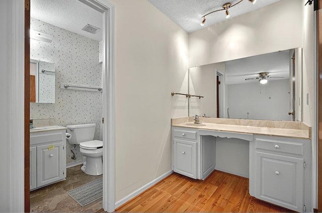 bathroom with ceiling fan, a textured ceiling, wood finished floors, vanity, and toilet
