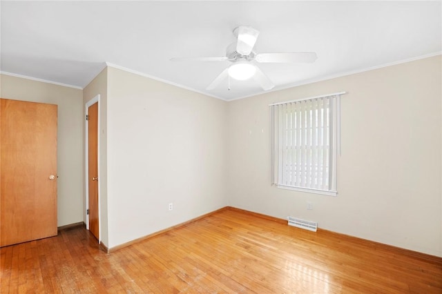 spare room featuring light wood-style floors, a ceiling fan, baseboards, visible vents, and ornamental molding