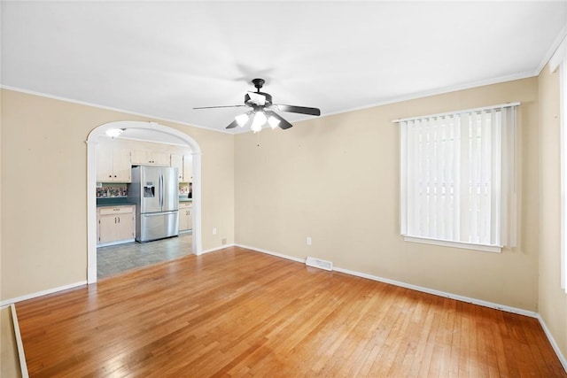 unfurnished room with light wood-style floors, arched walkways, a ceiling fan, baseboards, and visible vents