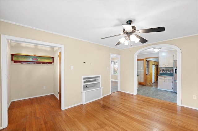 unfurnished living room with arched walkways, ceiling fan, baseboards, and light wood finished floors
