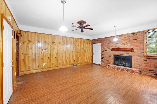 unfurnished living room featuring a ceiling fan, a brick fireplace, wood finished floors, and wooden walls