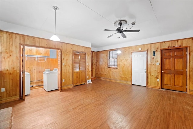 unfurnished living room featuring wooden walls, ceiling fan, light wood-style flooring, and washer / clothes dryer