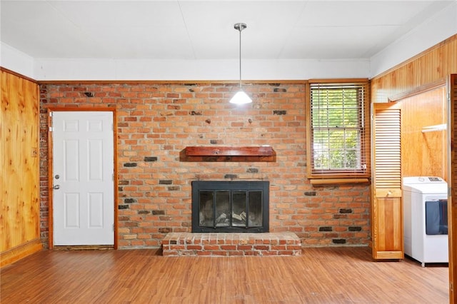 unfurnished living room with a brick fireplace, wood walls, washer / clothes dryer, and wood finished floors