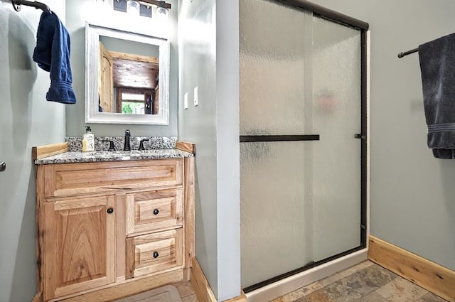 full bathroom with vanity, baseboards, stone finish flooring, and a stall shower