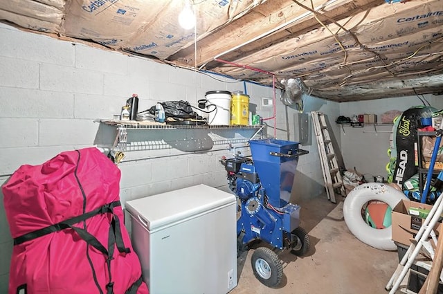 unfinished below grade area featuring concrete block wall, electric panel, and fridge