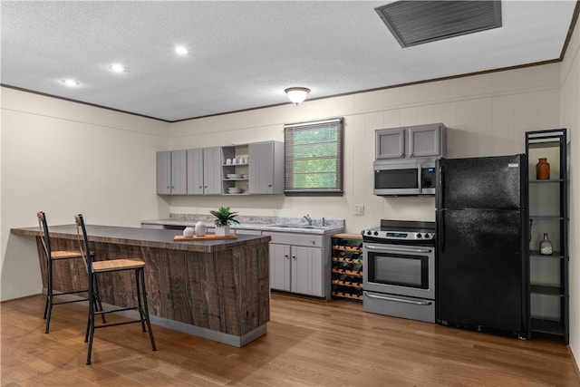 kitchen with gray cabinetry, appliances with stainless steel finishes, visible vents, and a kitchen bar
