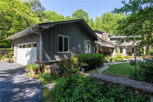 view of side of home featuring board and batten siding, an attached garage, and aphalt driveway
