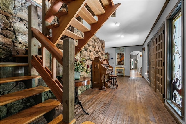 stairway featuring crown molding, arched walkways, baseboards, and hardwood / wood-style floors