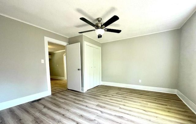 unfurnished bedroom with crown molding, a closet, wood finished floors, baseboards, and ceiling fan