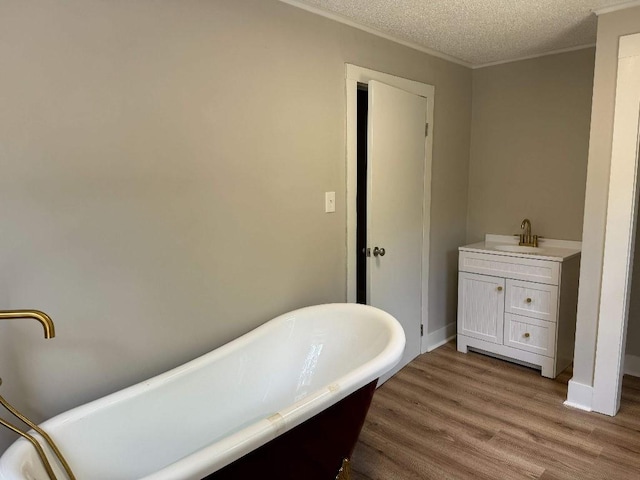 bathroom featuring a textured ceiling, crown molding, wood finished floors, vanity, and a soaking tub