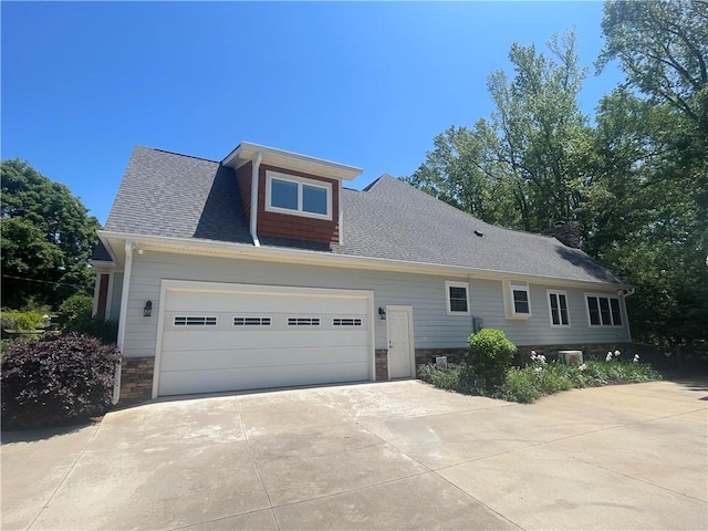 view of front facade with a shingled roof, an attached garage, concrete driveway, and stone siding