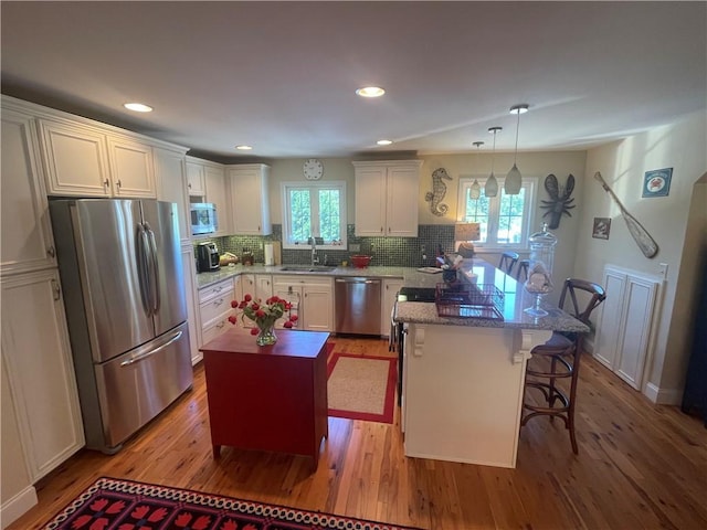kitchen with decorative backsplash, a peninsula, wood finished floors, a sink, and stainless steel appliances