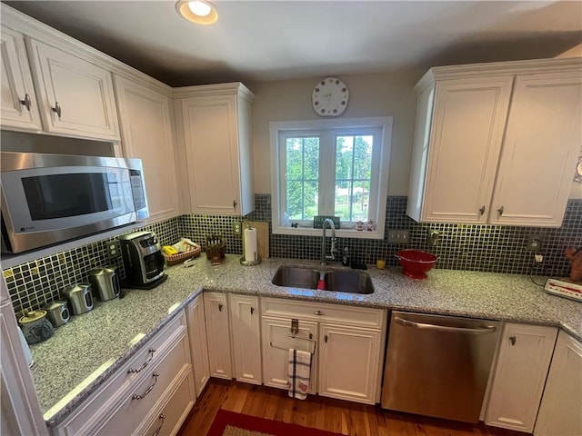 kitchen featuring decorative backsplash, dark wood-style floors, white cabinetry, a sink, and stainless steel appliances