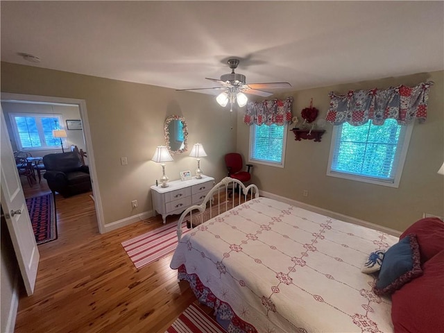 bedroom featuring baseboards, multiple windows, a ceiling fan, and wood finished floors