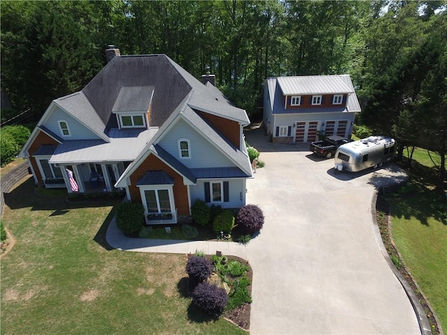view of front of house featuring a forest view, a chimney, metal roof, a front yard, and concrete driveway