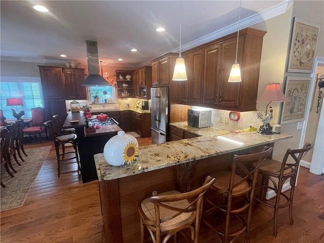 kitchen with high end refrigerator, light stone counters, crown molding, and island exhaust hood