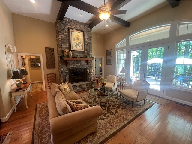 living room featuring a stone fireplace, baseboards, a high ceiling, and hardwood / wood-style floors