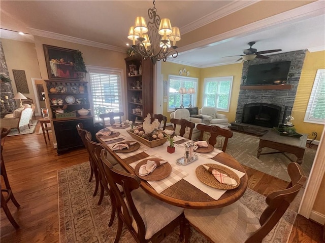 dining room featuring ornamental molding, a fireplace, ceiling fan with notable chandelier, and wood finished floors