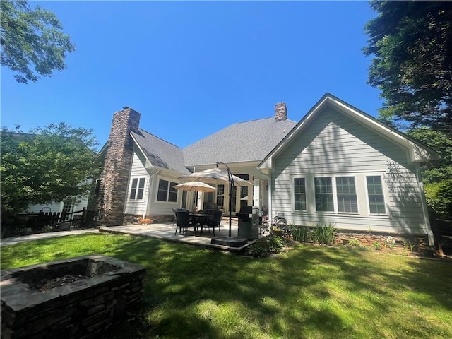 back of property with a lawn, a chimney, a patio area, and an outdoor fire pit